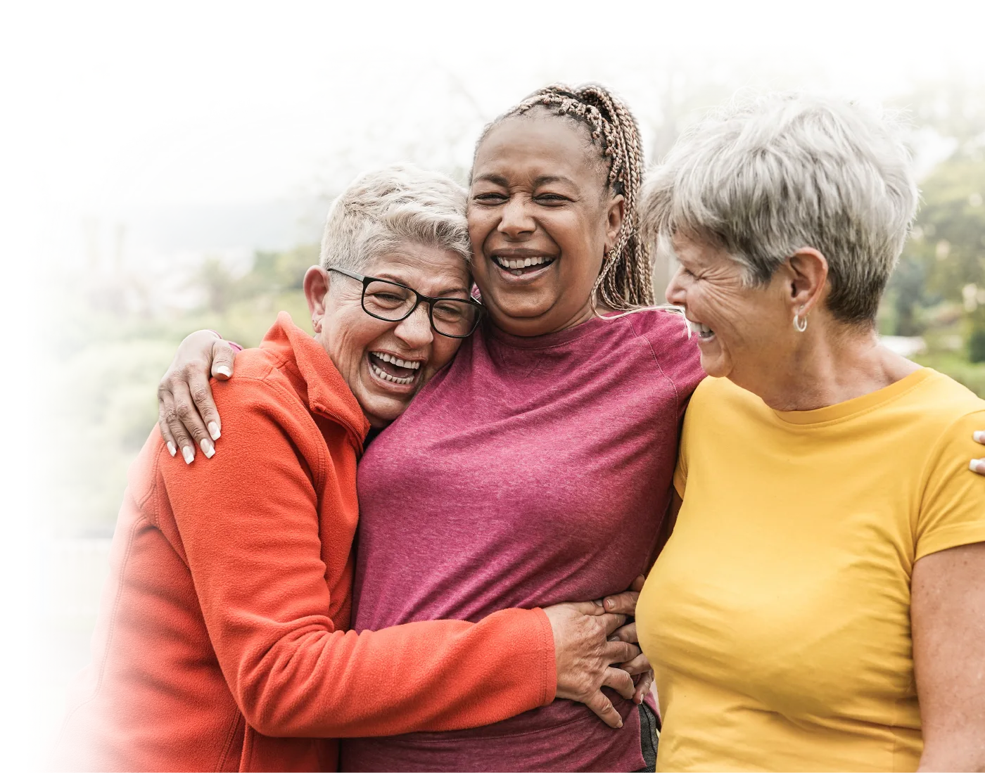 Photo of three older women smiling and in a friendly embraced with each other.